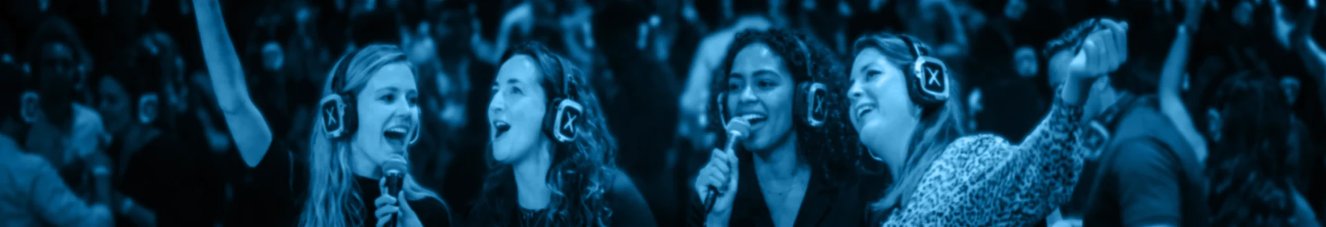 4 vrouwen die op een feestje met silent disco koptelefoons op aan het karaoke-zingen zijn.